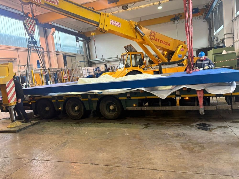 Crane placing a steel floor element off a flatbed trailer inside a production hall
