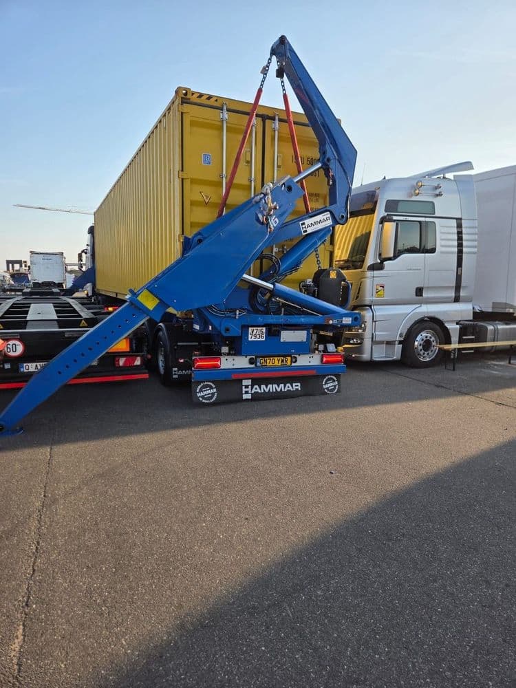 Rückansicht eines blauen Hammar-Sideloaders, der einen gelben 40-Fuß-Container mit Ketten und Gurten anhebt