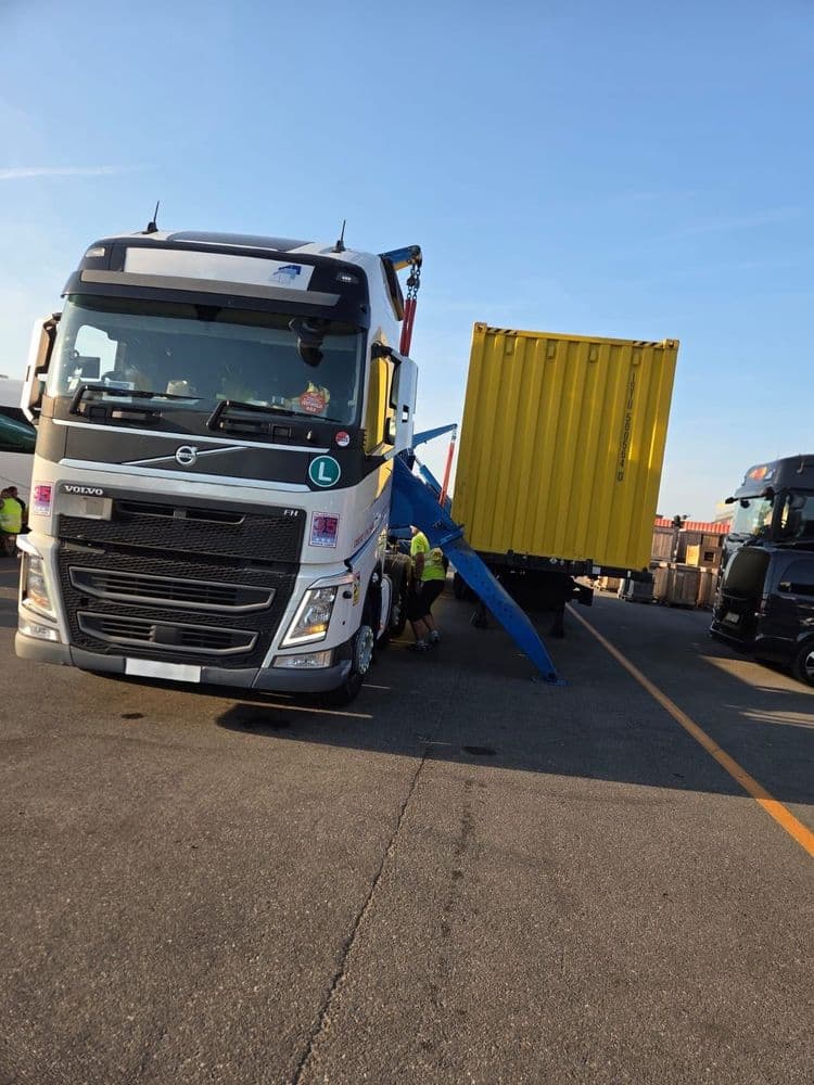 Sideloader hinter einer Volvo-Zugmaschine setzt einen gelben 40-Fuß-Container auf den Auflieger, Stützen am Boden