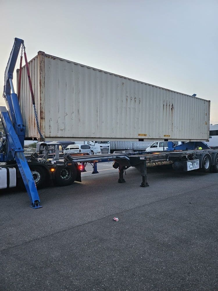 Beiger 40-Fuß-High-Cube-Container hängt an Ketten und Gurten eines Sideloaders über einem Containerchassis