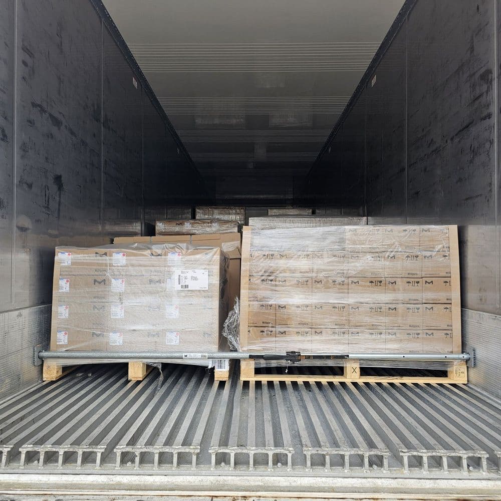 Deux palettes filmées de cartons sur palettes bois, sécurisées par une barre d'arrimage dans une semi-remorque